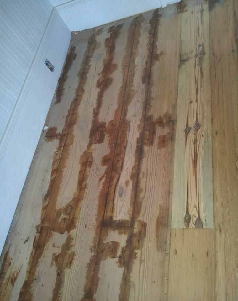 Wooden floor with dark stains running lengthwise between planks, near a white wall.