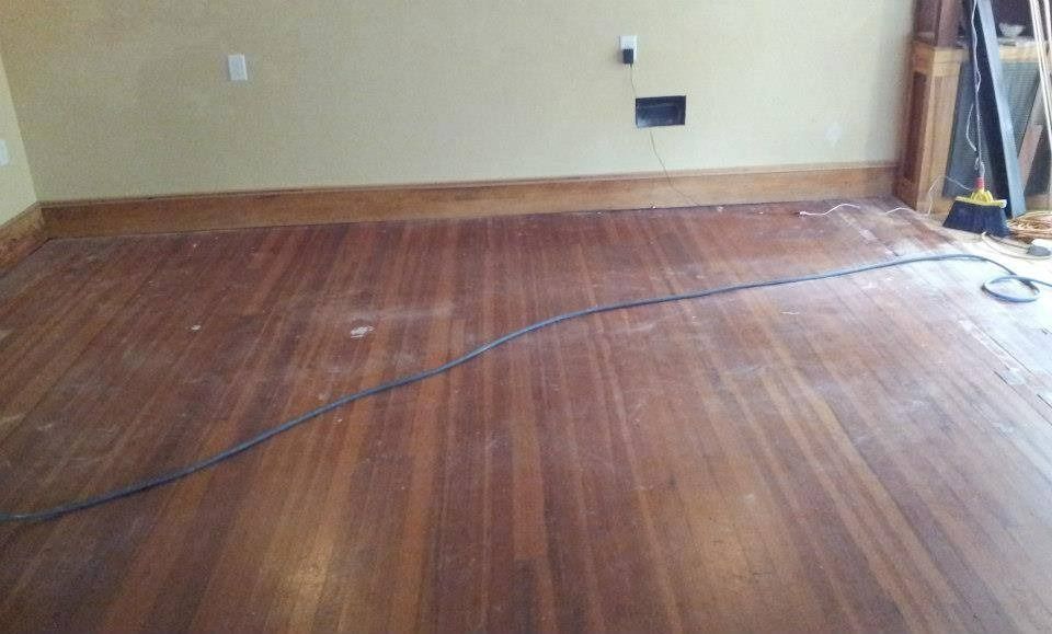 Hardwood floor with brown wooden trim, beige wall. A black cord lies across the floor.