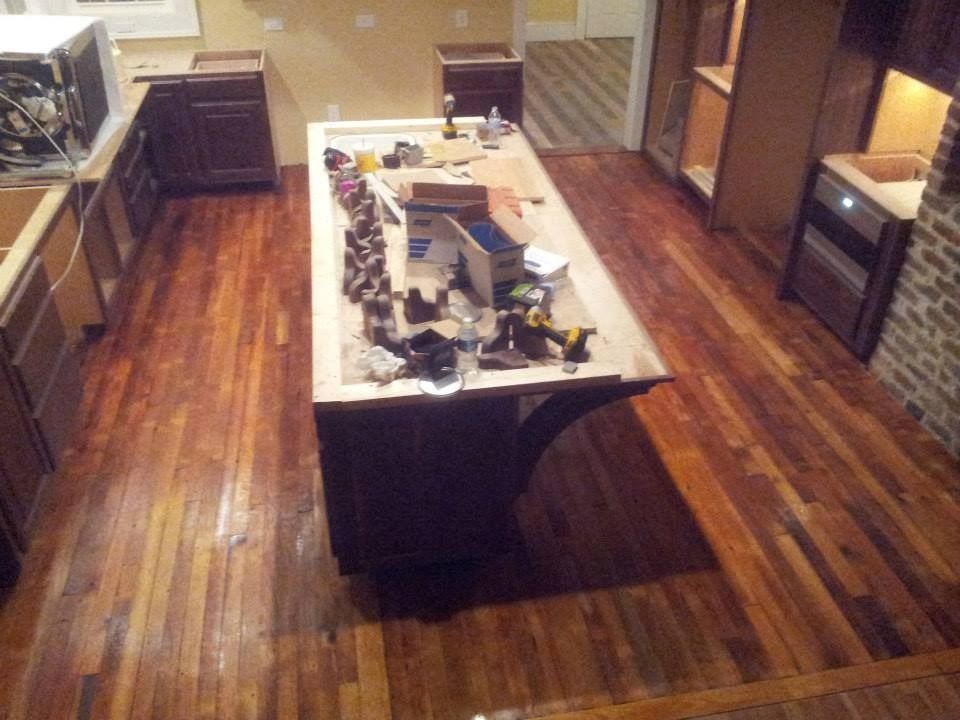 Kitchen renovation in progress: wood floors, dark cabinets, island with tools, open cabinets.