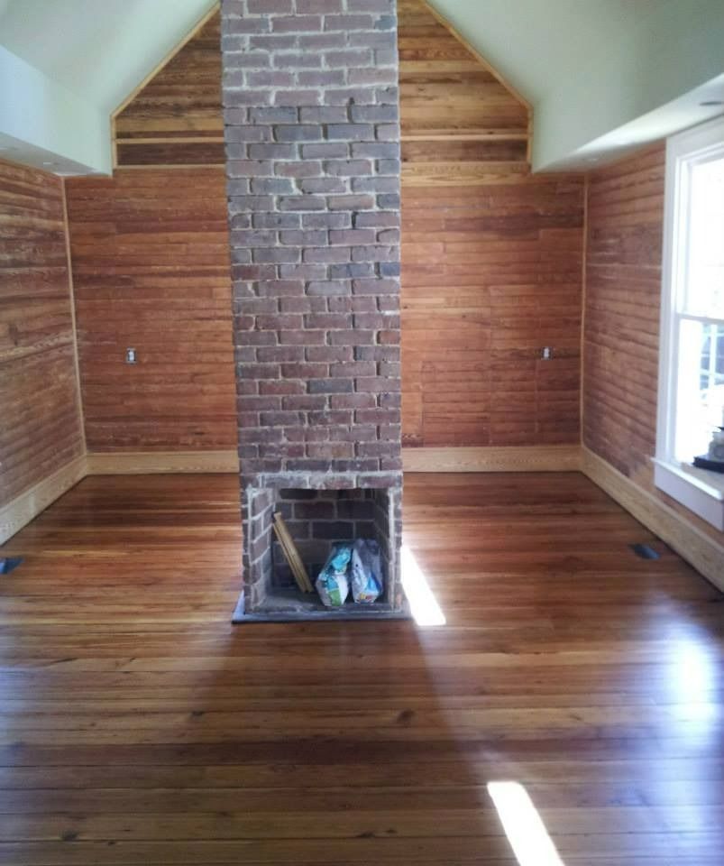 Room with brick fireplace, wood floors, and paneled walls. Sunlight streams through a window.
