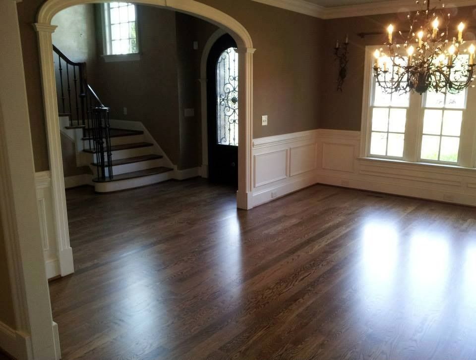 Empty room with wood floor, brown walls, white trim, staircase, and chandelier.