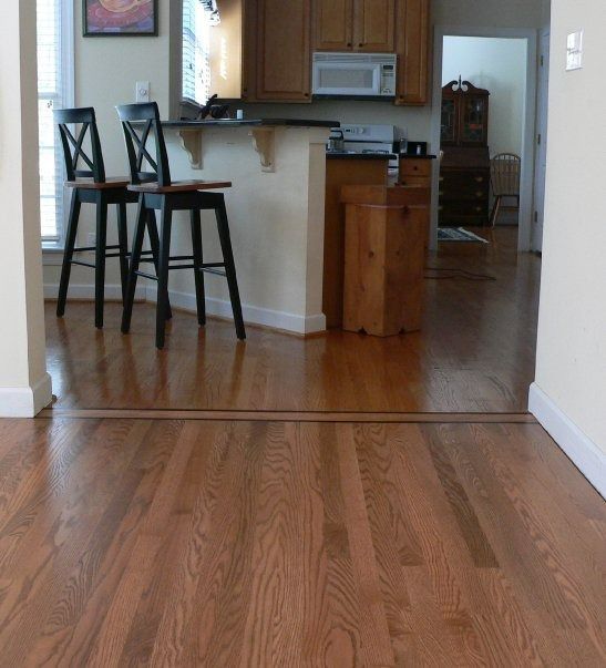 Hardwood floors lead to a kitchen with a counter, bar stools, and a microwave.