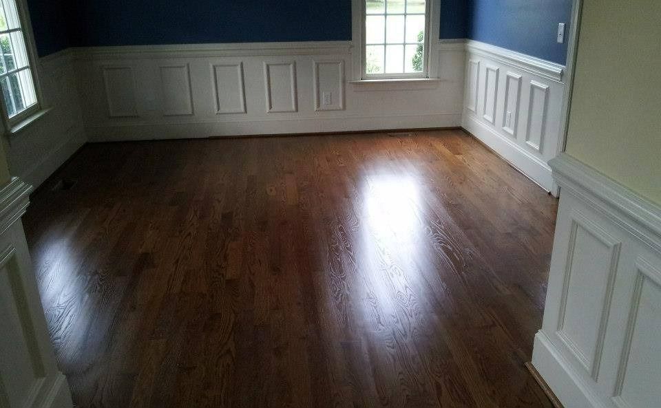 Dark wood floor in a room with white paneling and blue walls; sunlight streams in.