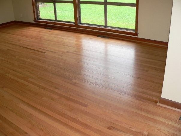 Shiny hardwood floor in an empty room with a window overlooking green grass.