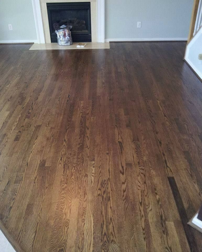 Dark brown hardwood floor in a room, with a fireplace and light blue walls in the background.