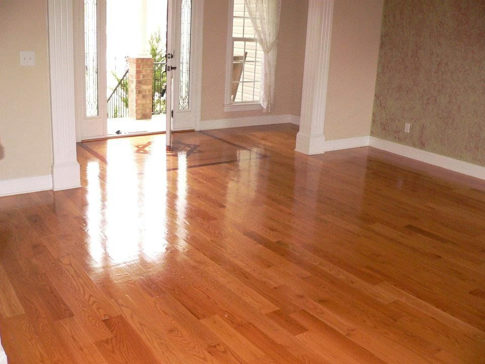 Shiny hardwood floor in an empty room with cream walls, a window, and open doorway.