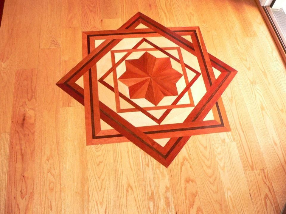 Wooden floor with inlaid geometric starburst design in shades of brown and tan.