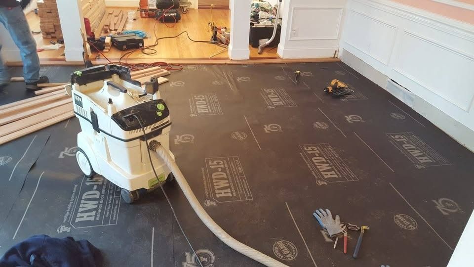 Floor renovation in progress, with a vacuum cleaner, protective underlayment, and tools in a house.