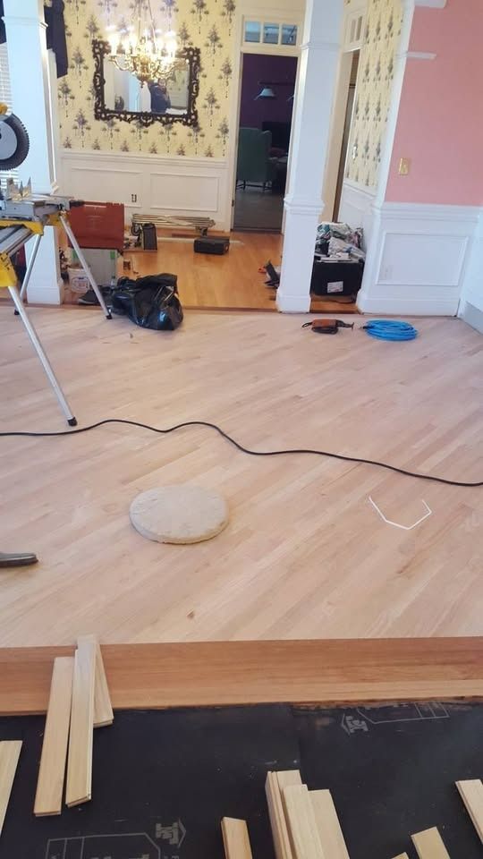 Hardwood flooring installation in progress; tools and materials scattered in a room with wallpaper and columns.