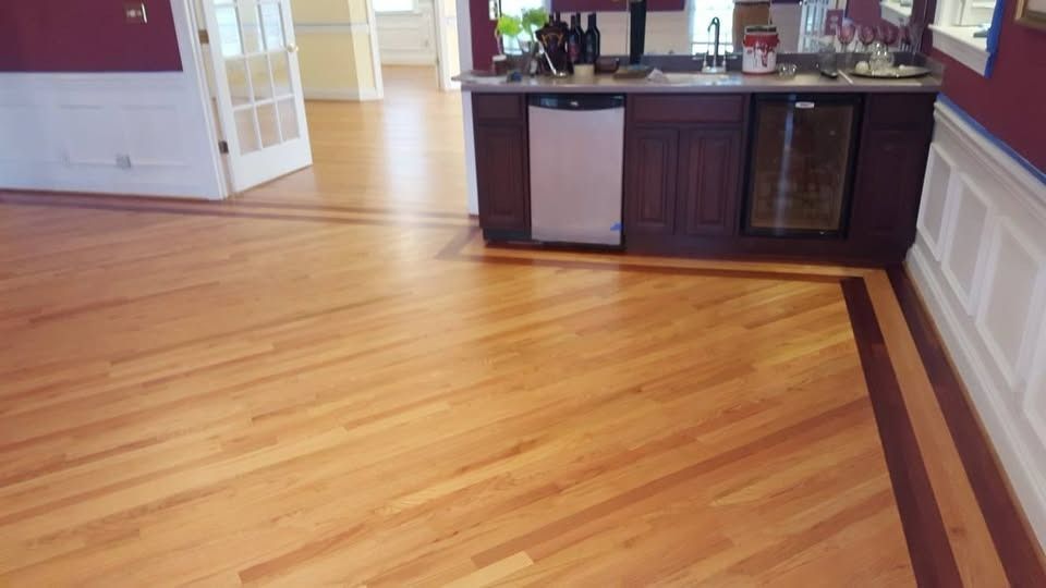 Wood floor with dark border, small bar with fridge and wine cooler, and white trim.