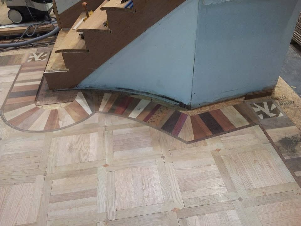 Wooden floor with inlaid border curving around stairs. Various wood tones and patterned squares.