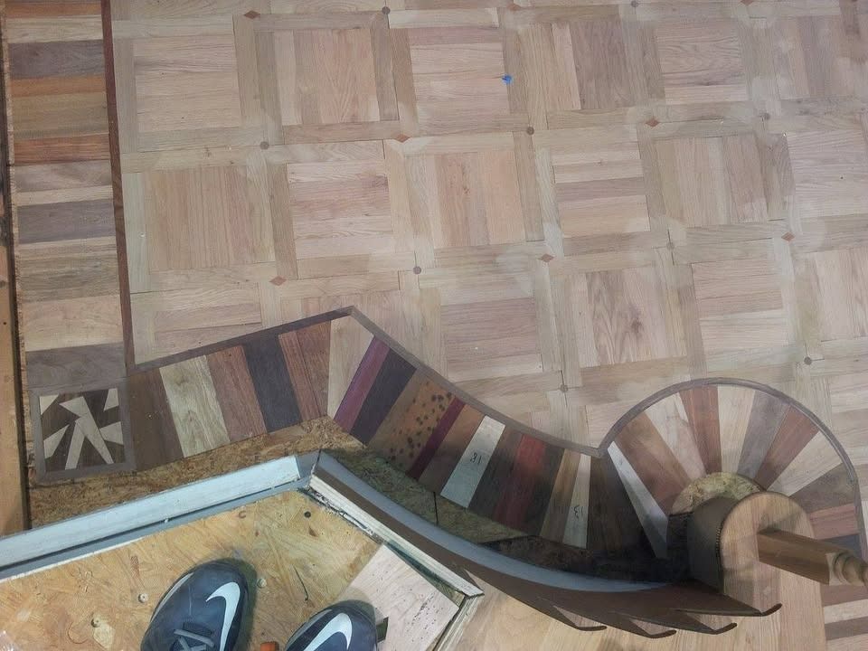 Wooden parquet floor with ornate border featuring colorful wood inlay and part of a person's feet wearing athletic shoes.