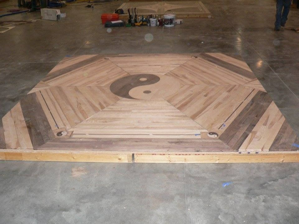 Wooden yin-yang symbol inlaid in a wood floor, with a light brown background and a dark yin-yang symbol.