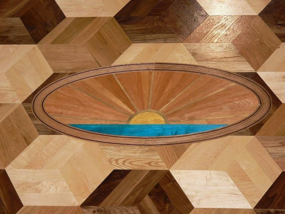 Wooden floor with a sunset mosaic in an oval frame.
