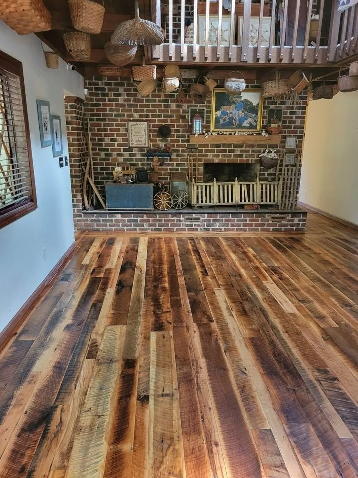 Rustic wood floor in a room with a brick fireplace and loft area, decorated with baskets and art.
