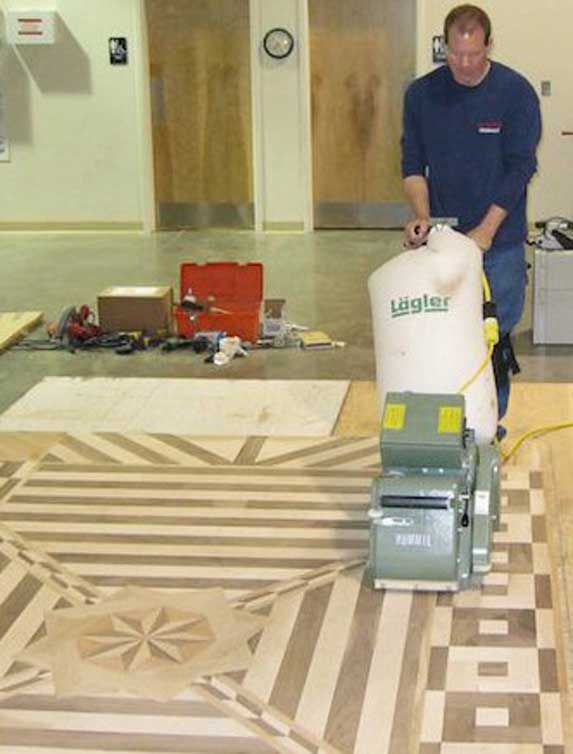 Man sanding intricate wooden floor pattern with machine. Indoor setting.