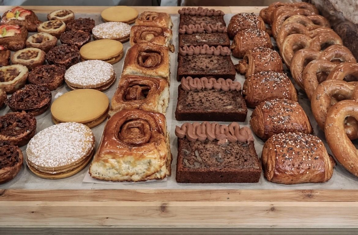 A wooden tray filled with a variety of freshly baked goods, including cinnamon rolls, brownies, cookies, and pretzels.