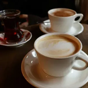 Two cups of latte with foam art and a glass of dark tea sit on a wooden table.