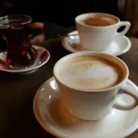 Two cups of latte with foam art and a glass of dark tea sit on a wooden table.