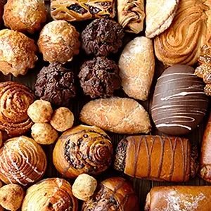 An assortment of various baked goods, including pastries, muffins, rolls, and chocolate-covered treats, on a dark surface.