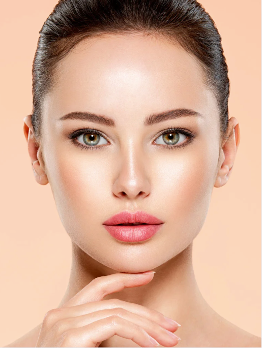 Woman with fair skin, styled hair, and makeup; hand near chin, on peach background.