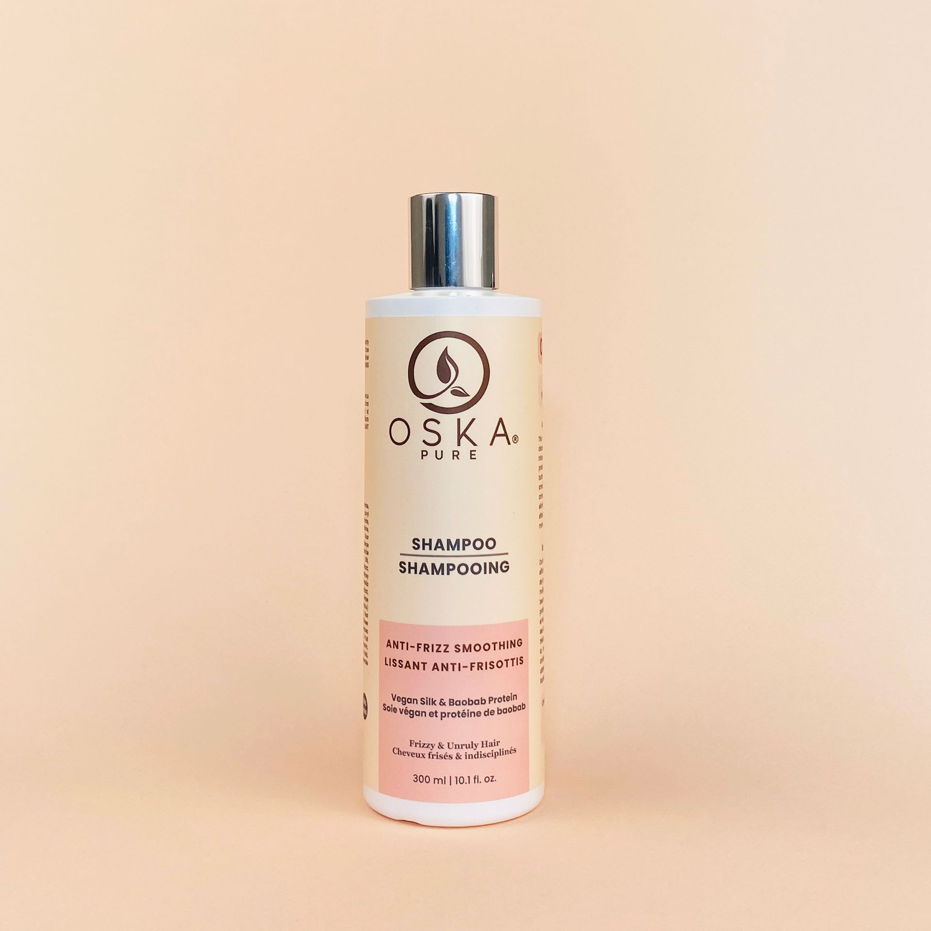 A bottle of OSKA shampoo with a silver cap, on a light peach background.