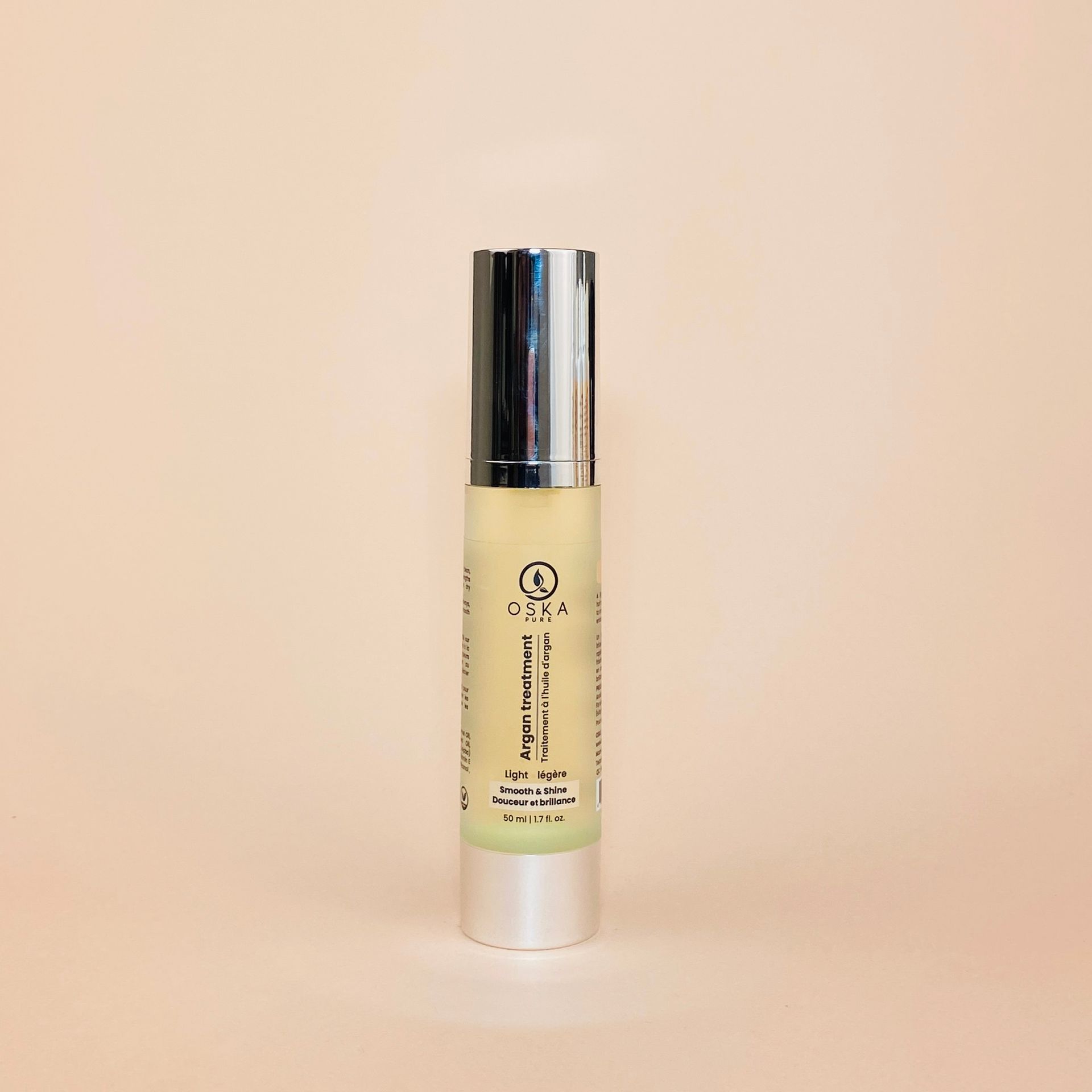 A cylindrical bottle of green liquid with a silver cap on a light peach background.