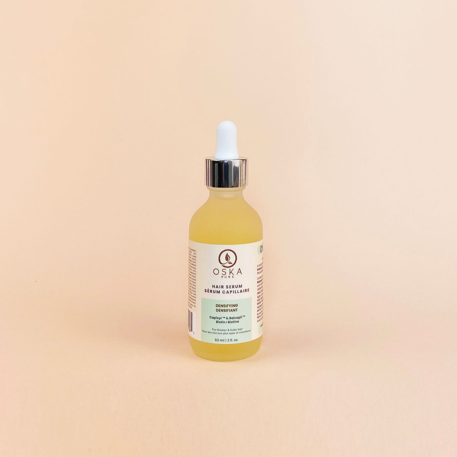 Bottle of yellow liquid skincare with white dropper and label on peach background.