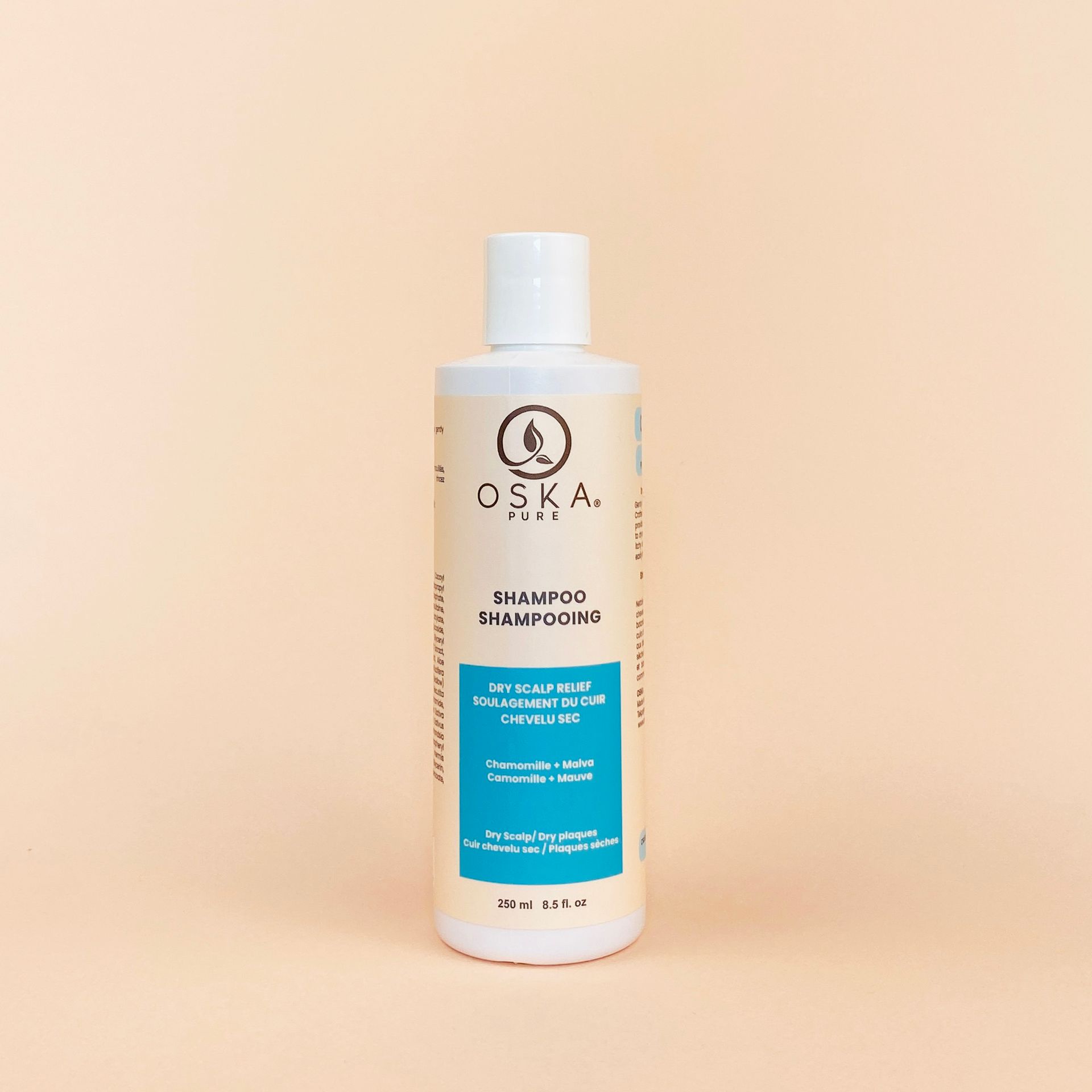 White shampoo bottle with blue label, text and a tree logo. Set against a peach background.