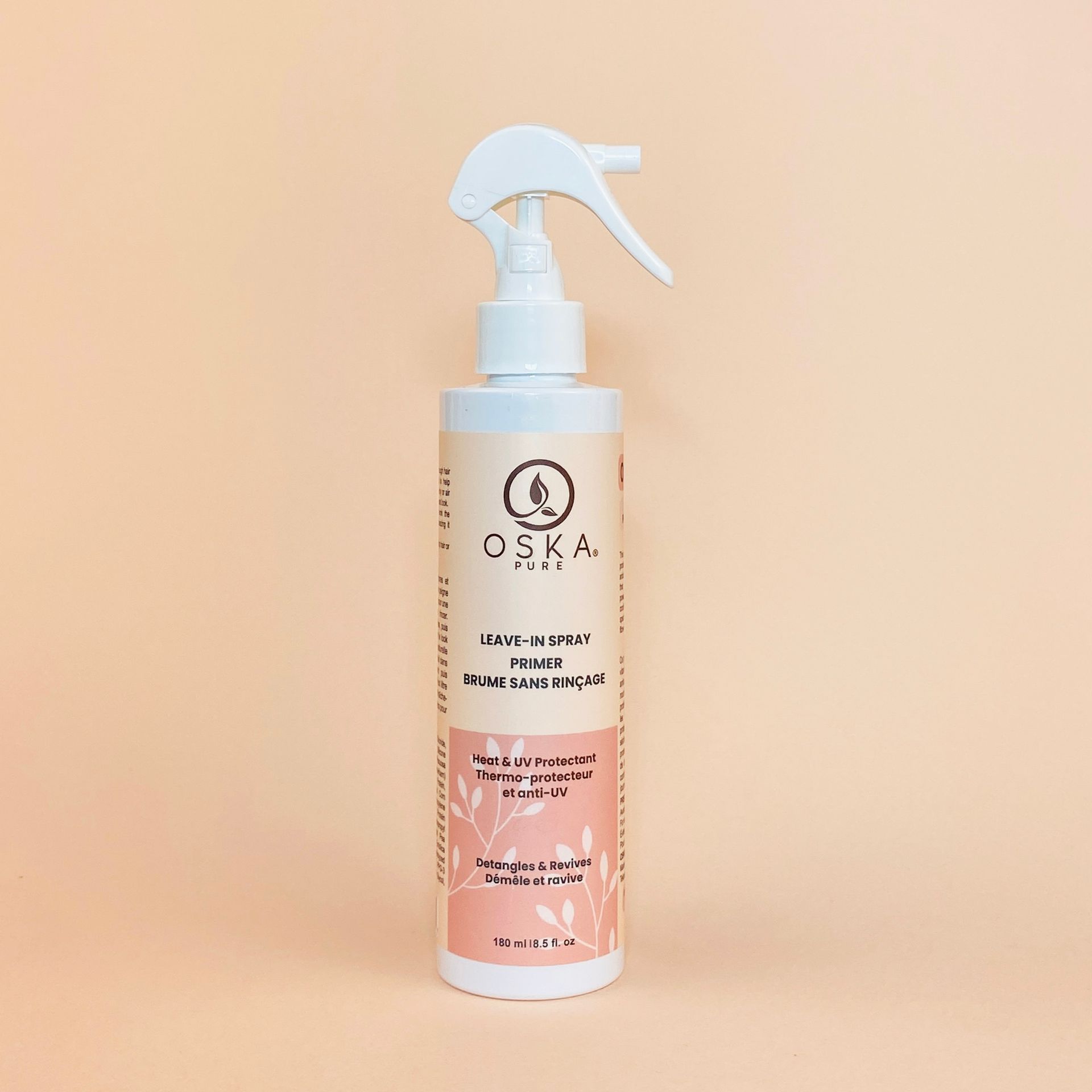 White spray bottle of OSKA hair product on a peach background.