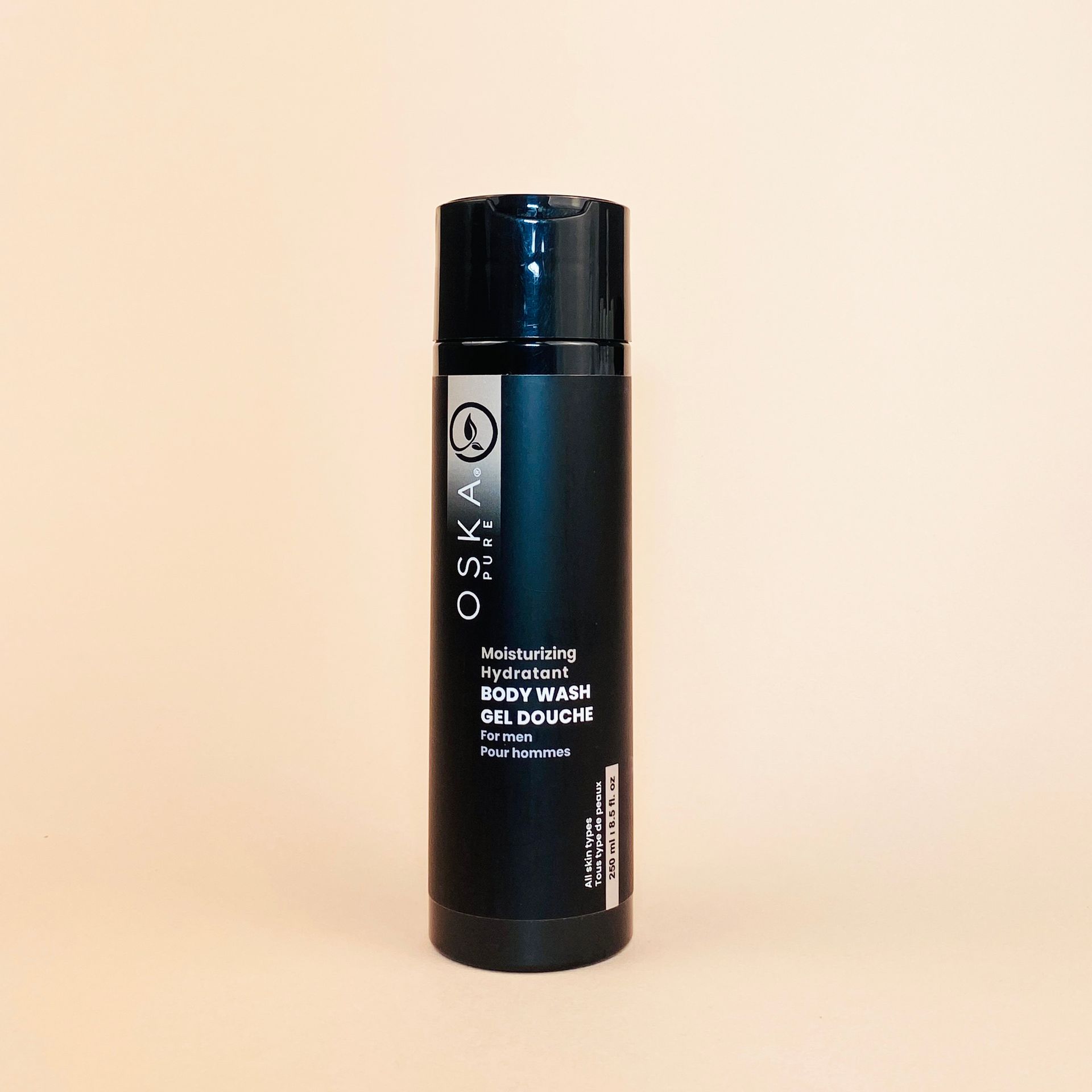 Black OSKA body wash bottle on a beige background.
