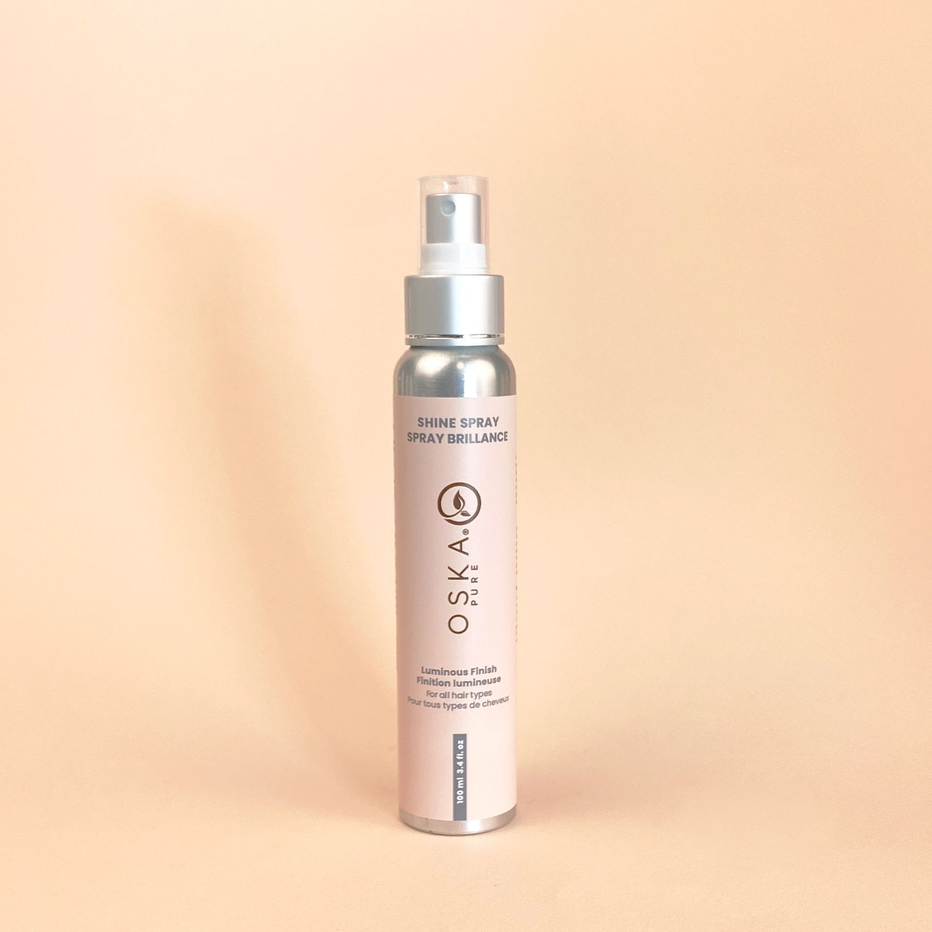 Spray bottle of OSKA skin product on a light peach background.