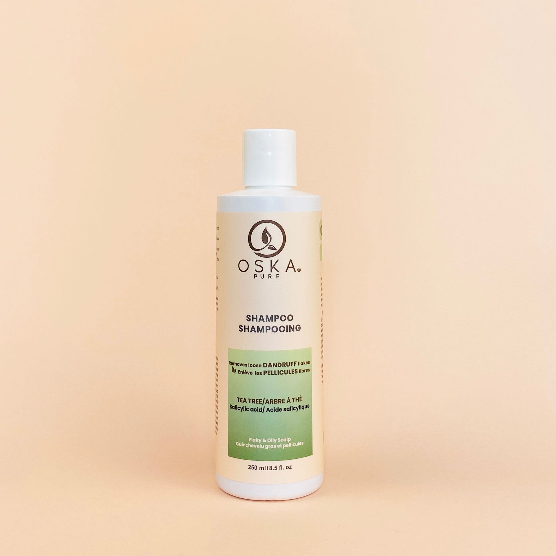 A bottle of OSKA shampoo on a beige background. It's white with green and beige labels.