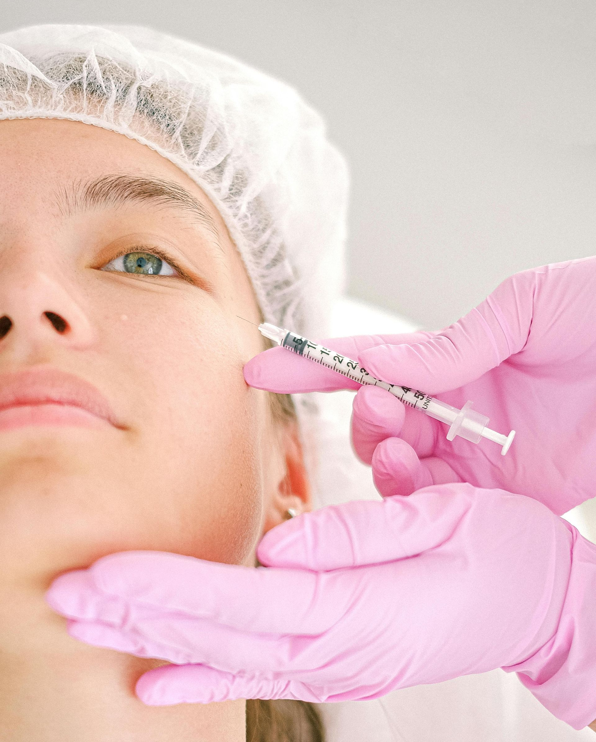 Person receiving a facial injection, held by gloved hand.  In medical setting.