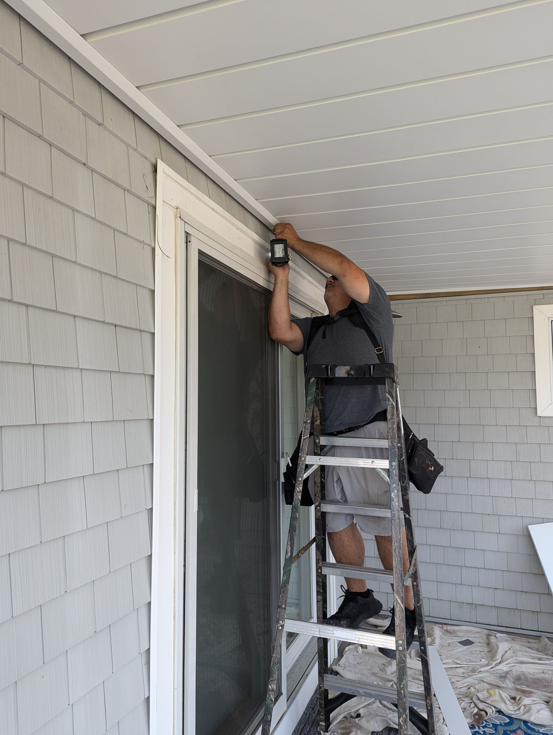 A man is standing on a ladder working on a sliding glass door.