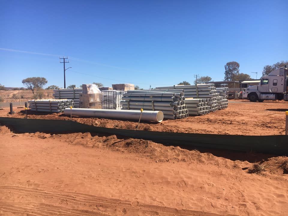 A Truck is Driving Down a Dirt Road Next to a Pile of Pipes — ASPLUM & CIVIL In Alice Springs, NT