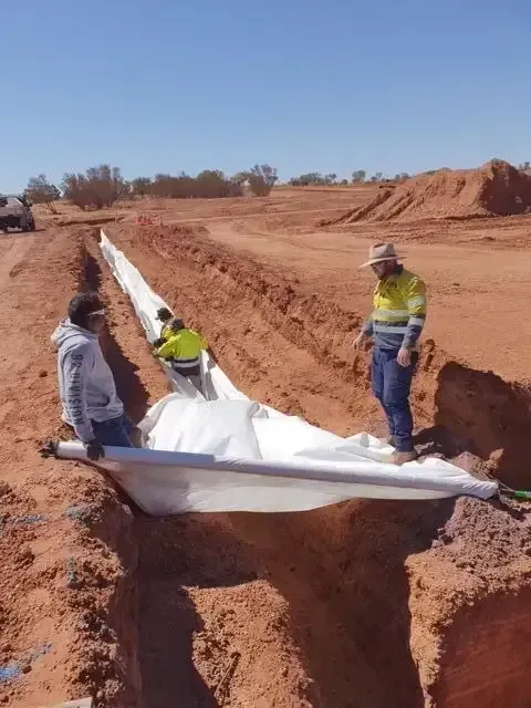 A Man Is Working in The Dirt Next to A Large Excavator — ASPLUM & CIVIL In Alice Springs, NT