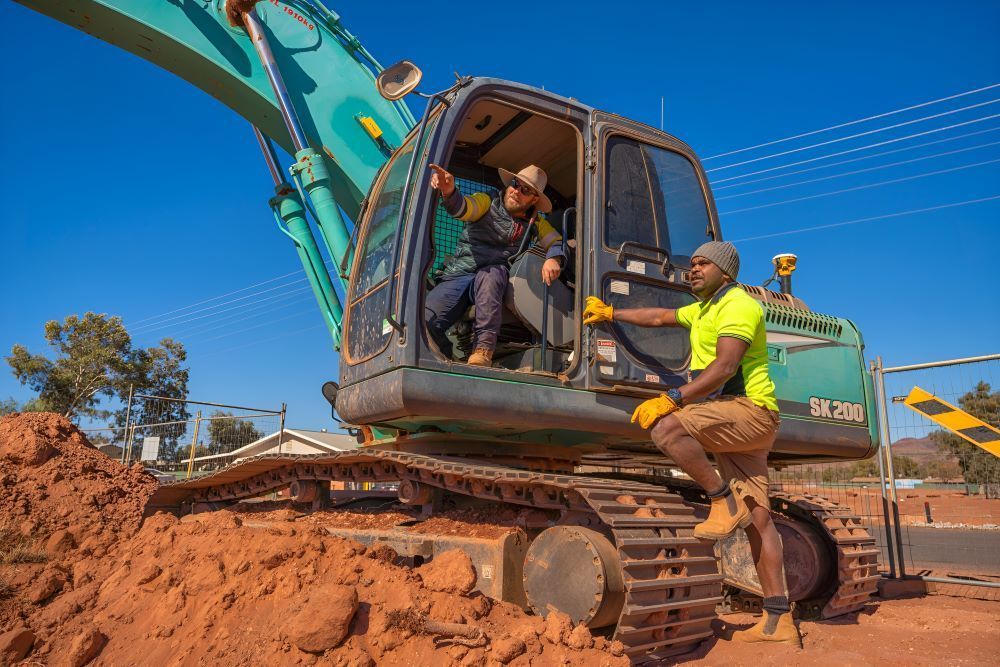 Two Men Are Sitting on The Back of A Large Excavator — ASPLUM & CIVIL in Alice Springs, NT