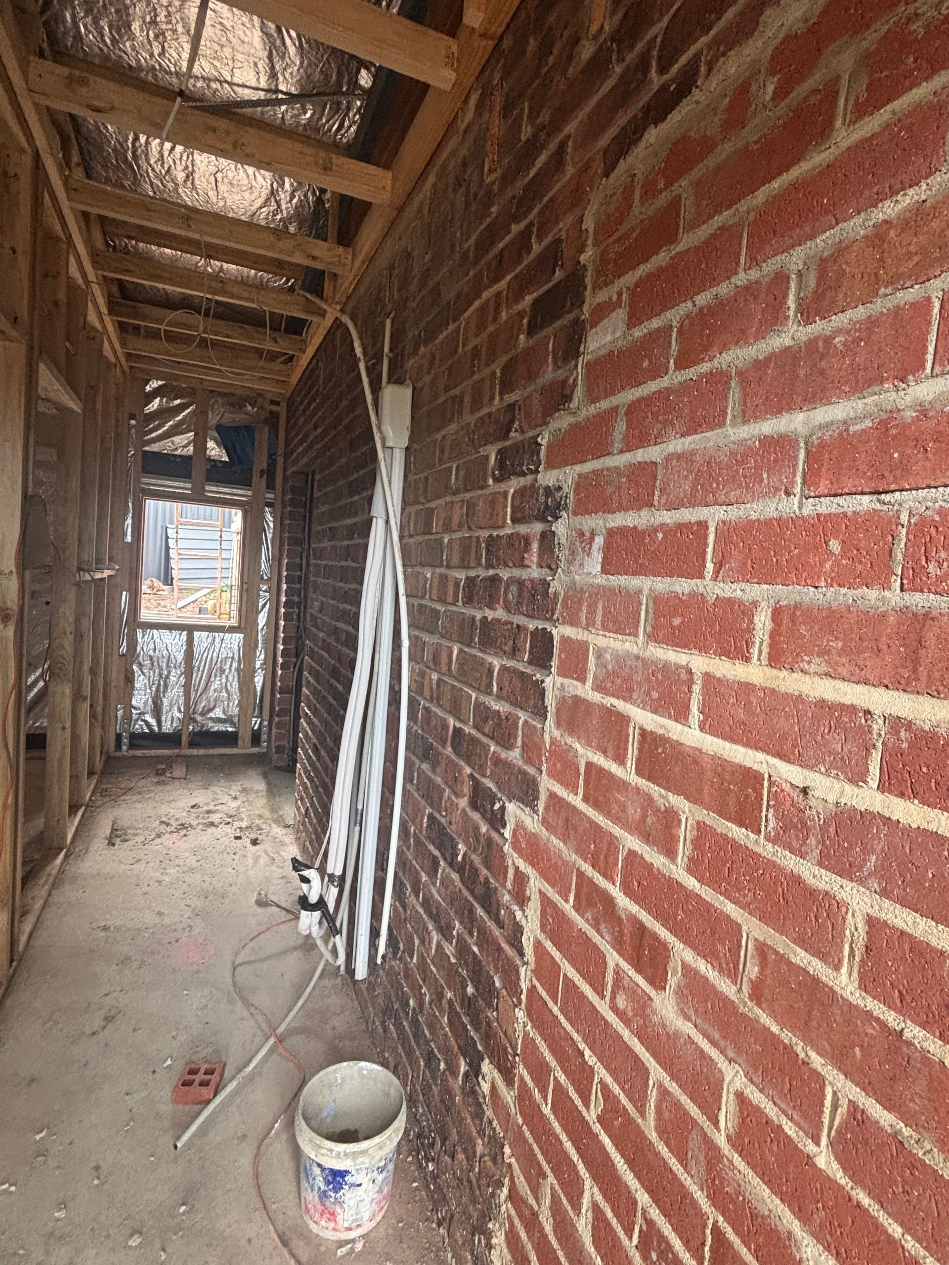 Construction of a narrow hallway with exposed wood framing and a red brick wall.