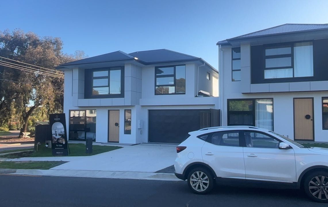 Two-story modern homes with white exterior and dark roofs; a white car parked on street in front.