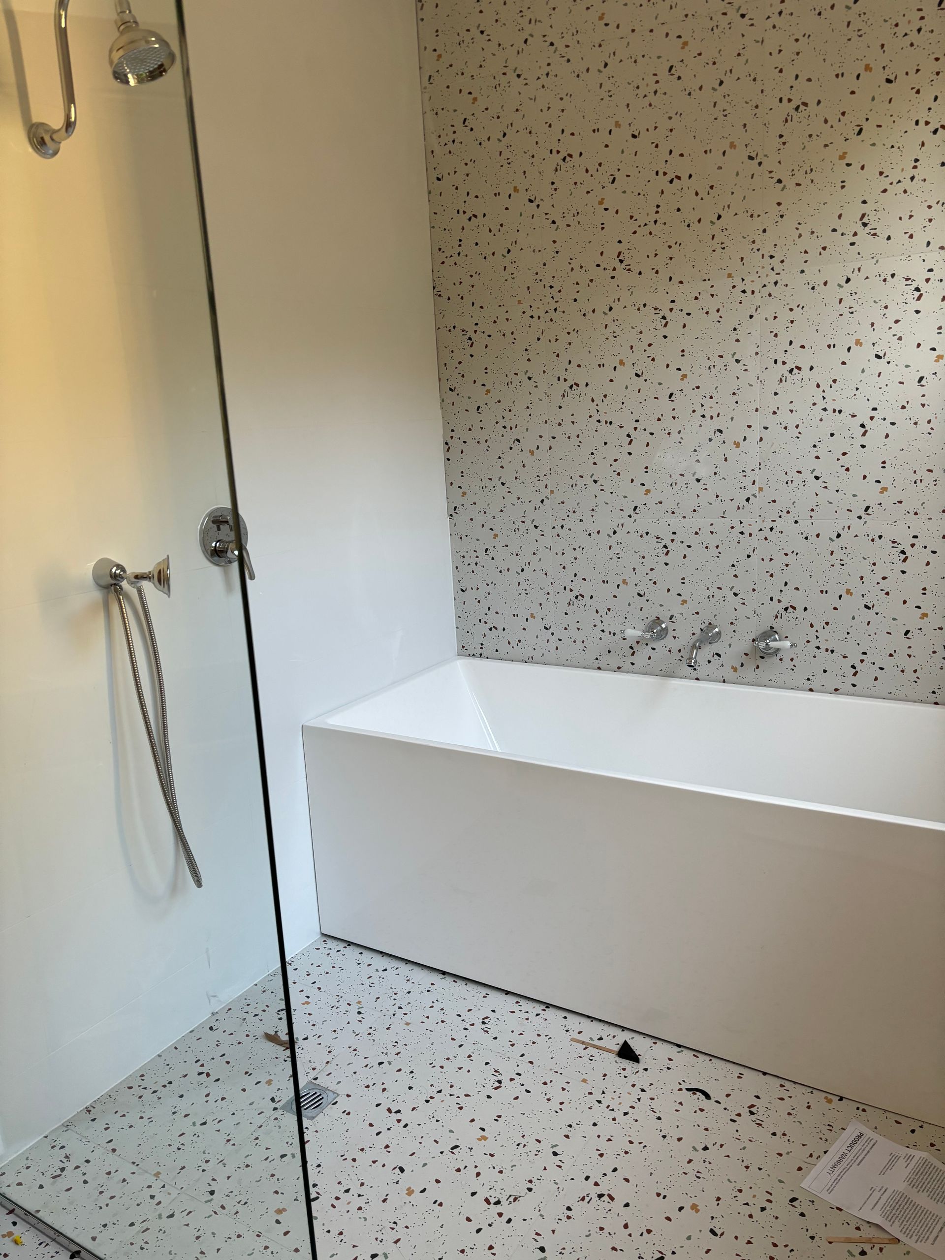 Modern bathroom with white tub, speckled gray and white tile, and glass shower door.