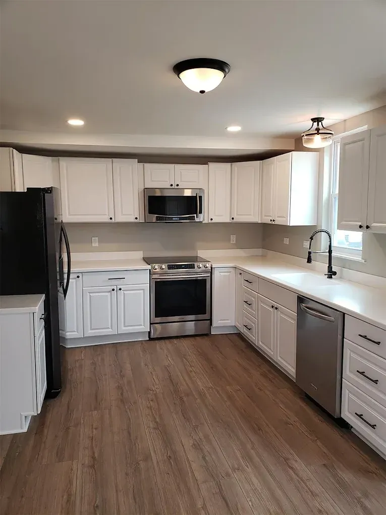 Modern kitchen with white cabinets, stainless steel appliances, and wood-look flooring.