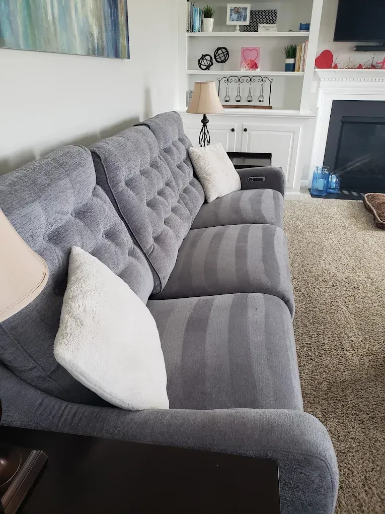 Gray tufted sofa with striped cushions and two white pillows, indoors with a fireplace and shelves.
