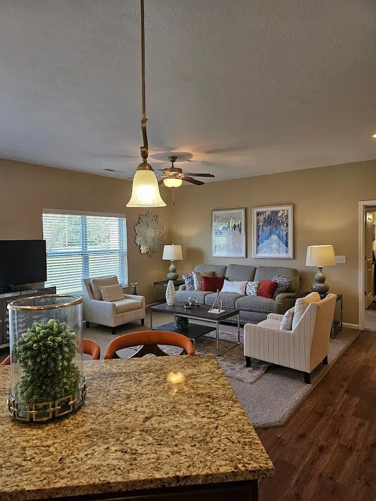 A modern living room with a gray sectional, two beige armchairs, neutral walls, a patterned rug, and a pendant light.