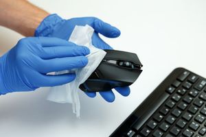 A person wearing blue gloves is cleaning a computer mouse with a cloth.