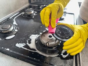 A person wearing yellow gloves is cleaning a gas stove with a cloth.