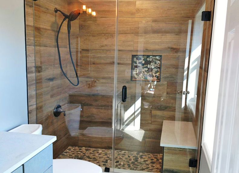 Modern bathroom shower with glass doors, wood-look tile walls, and a black rainfall showerhead.