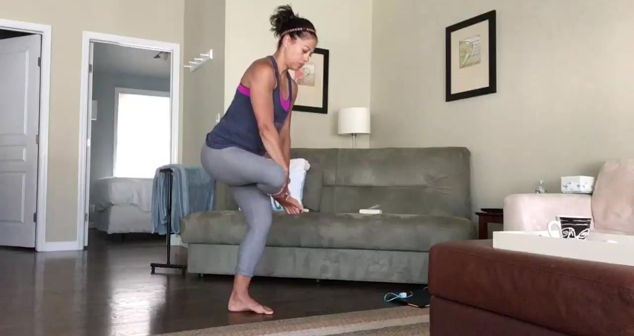 Woman stretches her leg, holding foot in hands, indoors.