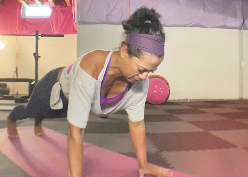 Woman doing a push-up on a pink mat in a home gym. She wears athletic attire and a headband.
