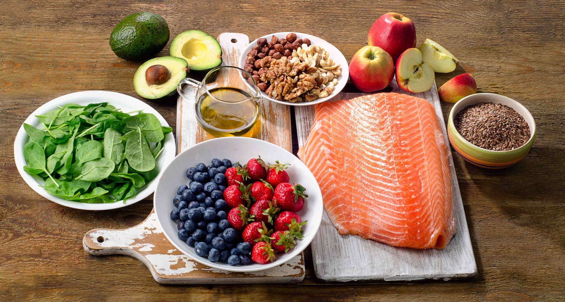 Healthy foods arrangement: salmon, avocado, berries, nuts, spinach, apples, seeds, and oil.